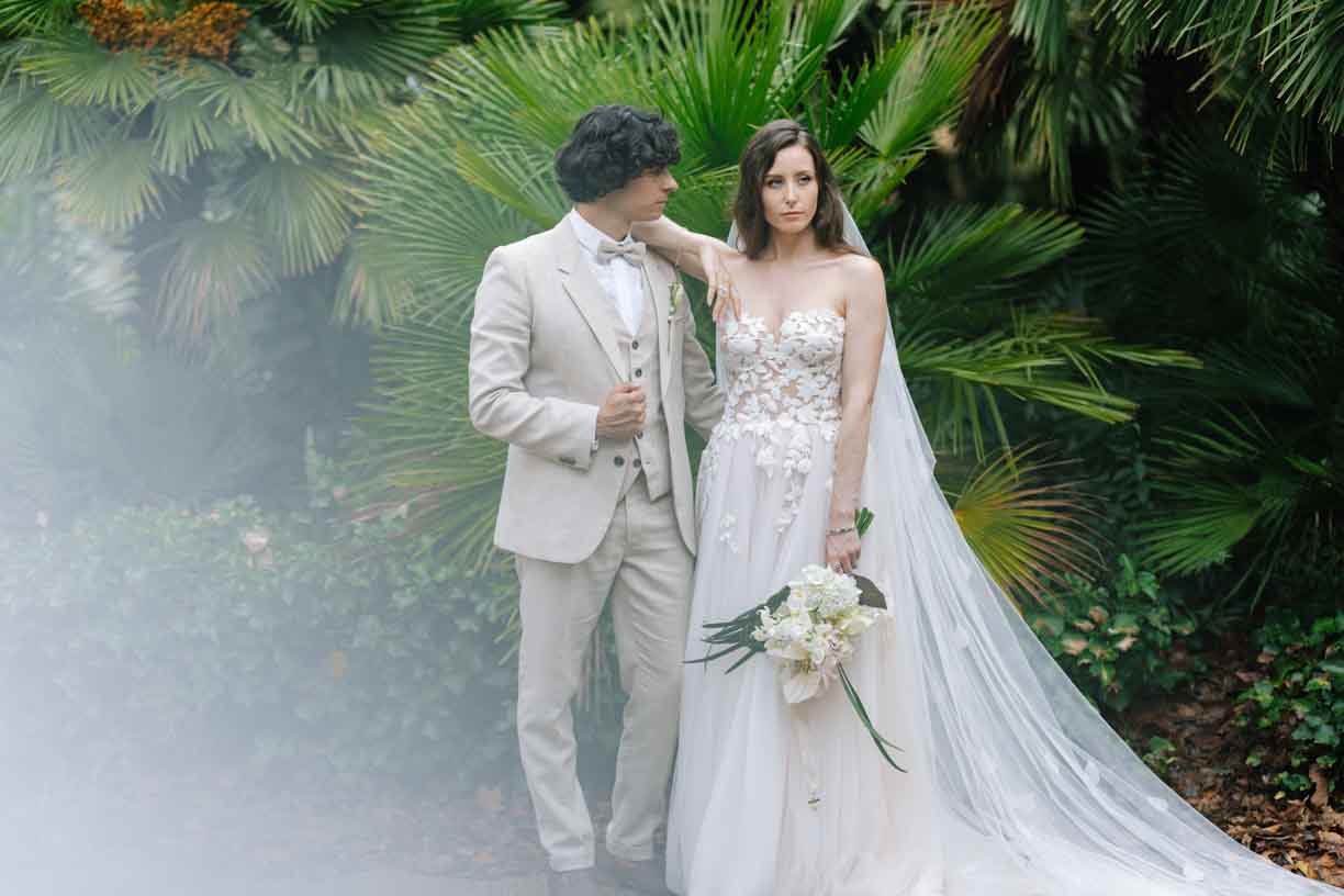 A bride and groom pose together in front of lush palm trees, capturing a moment of love and celebration.